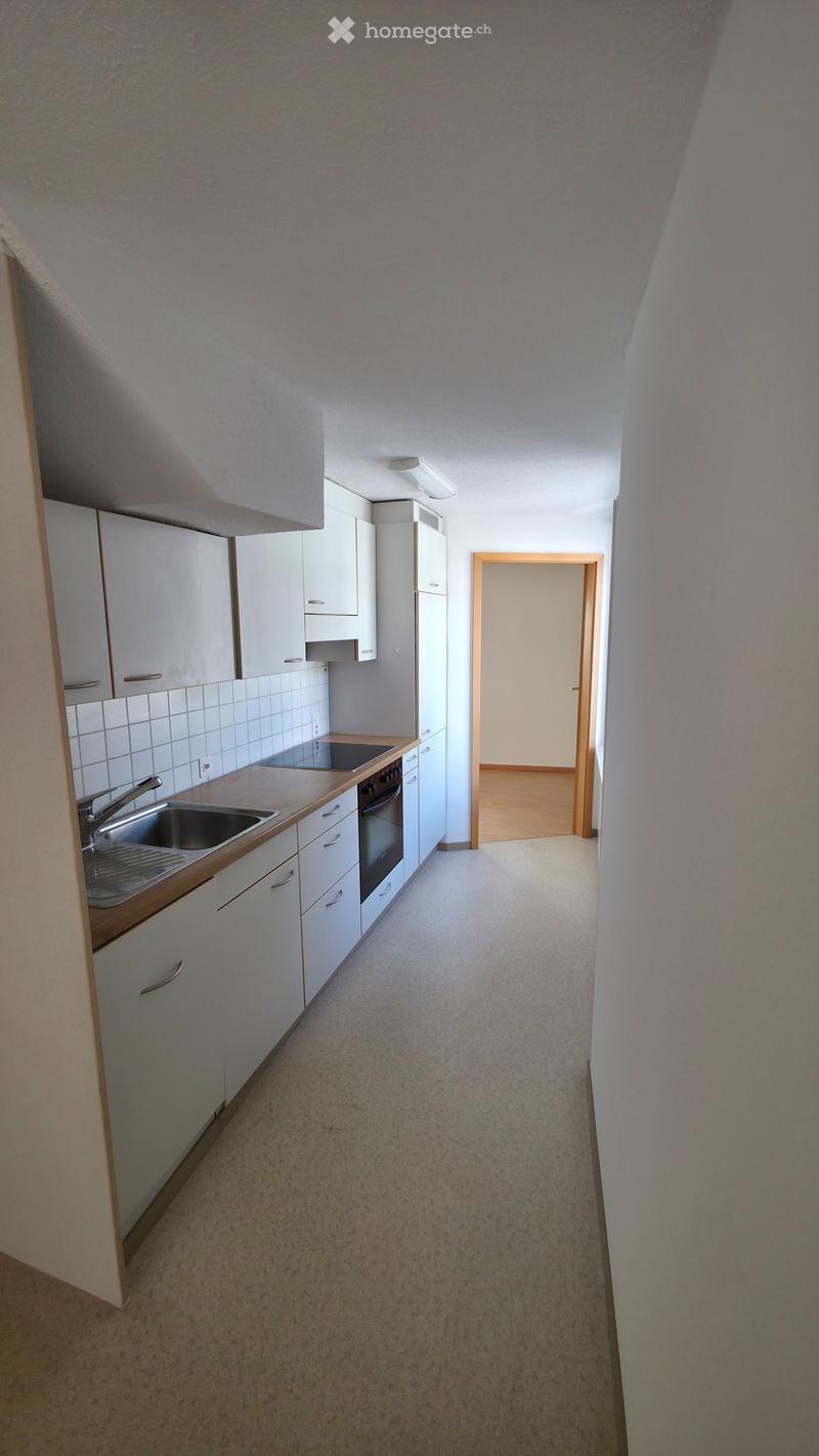 Modern kitchen with white cabinets, a sink, and an oven, leading to a hallway with wooden flooring.