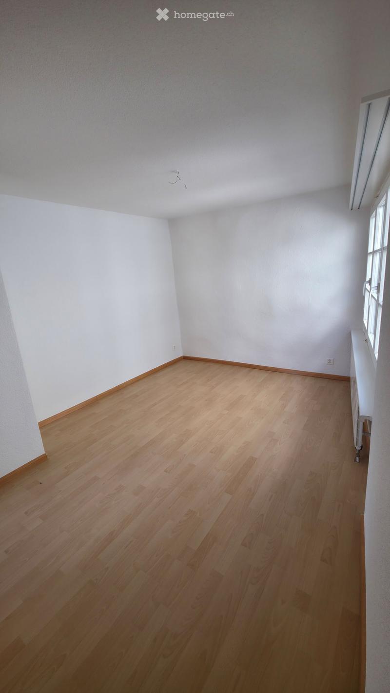Empty room with light wooden flooring and white walls, featuring a window on one side and a radiator below it.