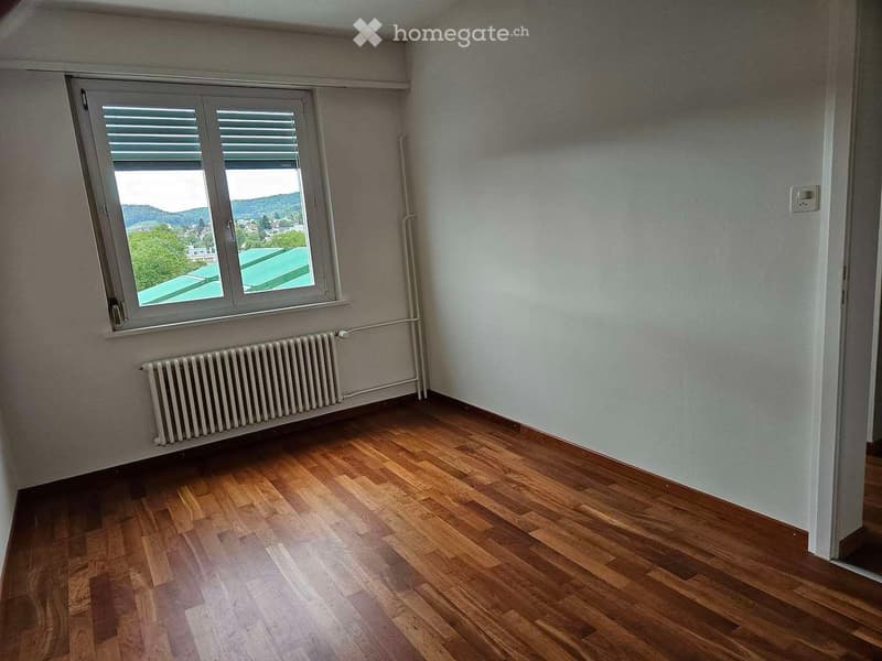 Empty room with wooden flooring, white walls, a window with blinds, and a radiator below the window.