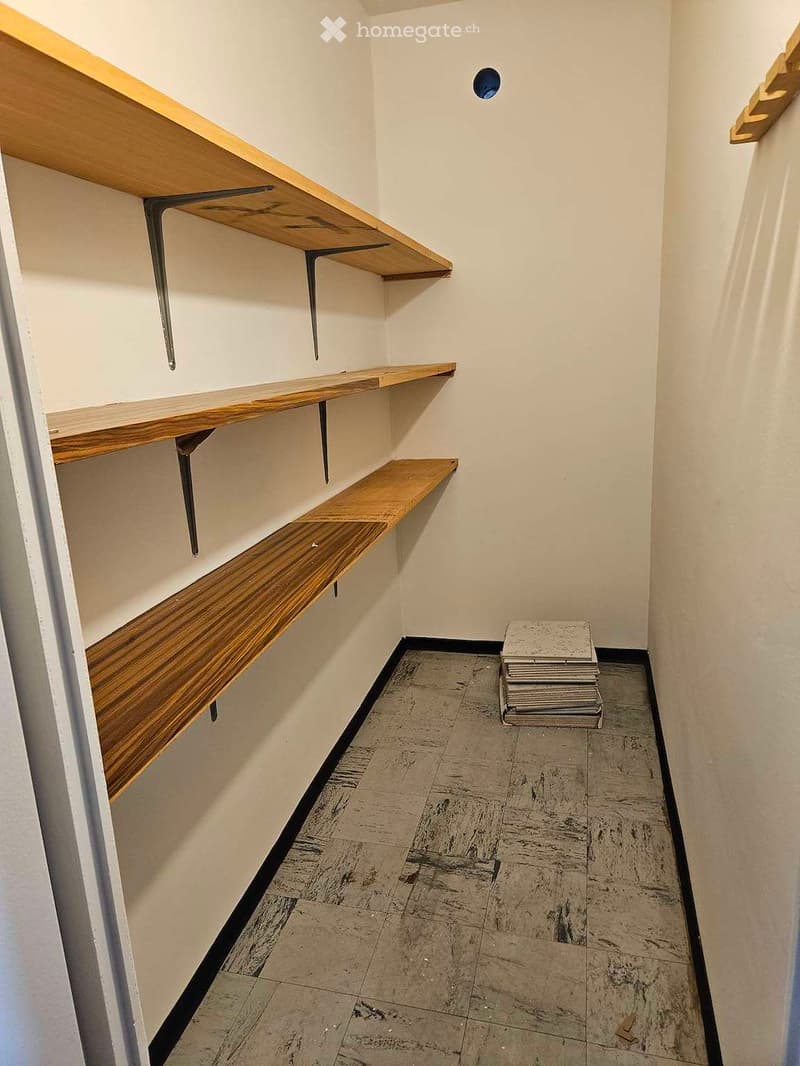Empty room with white walls, wooden shelves, and a stack of folded blankets on the floor.