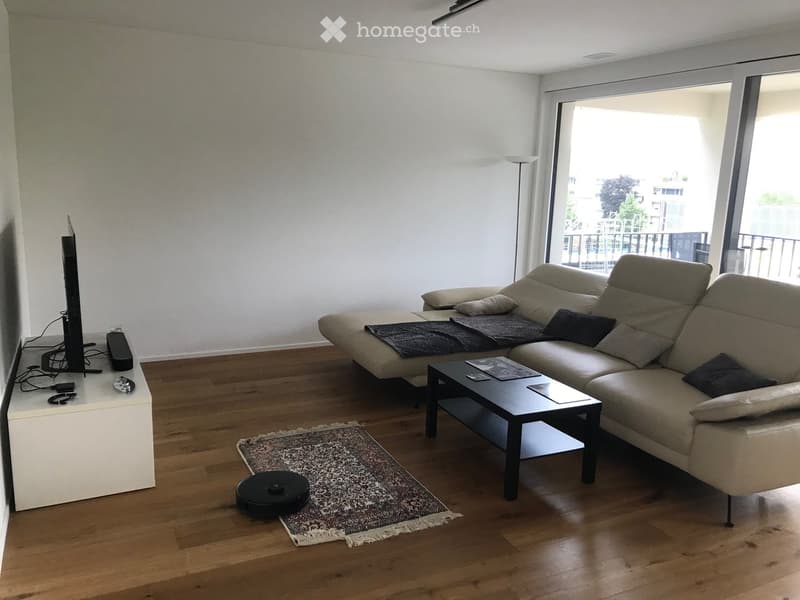 Modern living room with a beige sectional sofa, coffee table, TV, and a large window leading to a balcony.