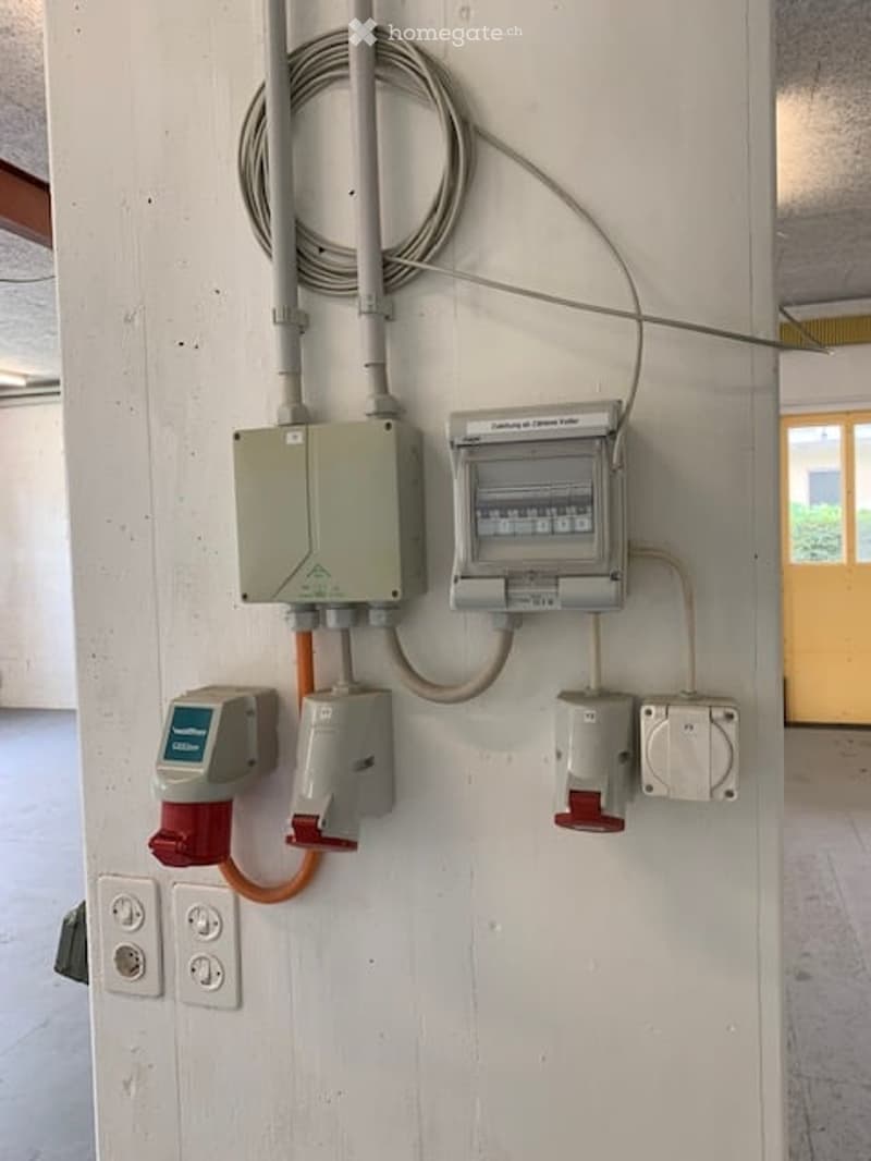 Empty room with electrical panels and wiring visible on a white wall. No furniture or equipment present.