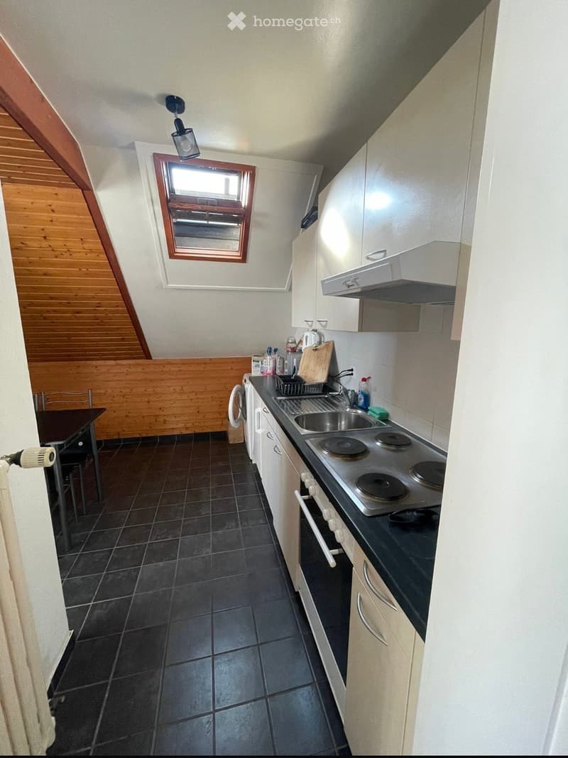 Modern kitchen with white cabinets, black countertop, electric stove, sink, and small dining area with a table and chairs. Features a skylight window and wooden accents on the walls.