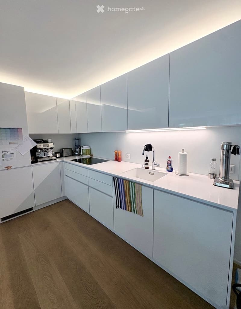 Modern kitchen with white cabinets, a central island, and various appliances including a coffee maker, toaster, and sink.