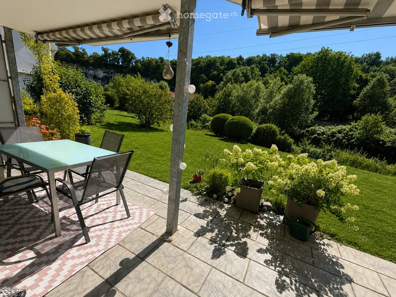 Balcony with a glass table, chairs, and a view of a well-maintained garden.