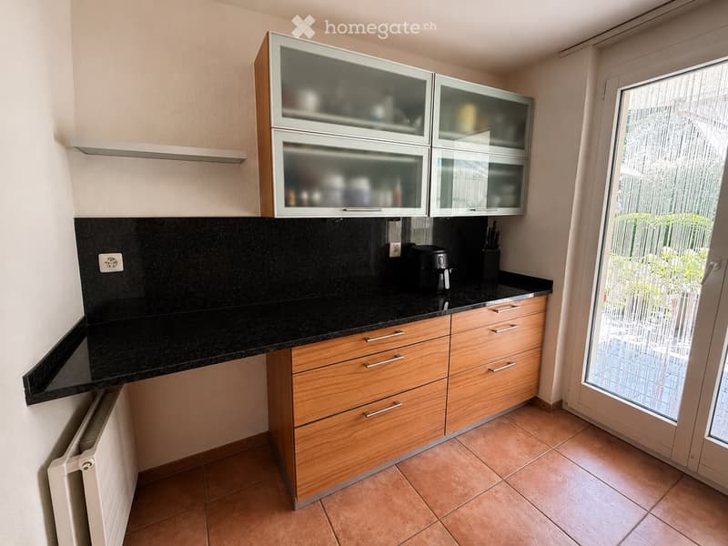 Modern kitchen with wooden cabinets, black granite countertop, and glass-fronted upper cabinets. Features a coffee maker and knife block on the counter.