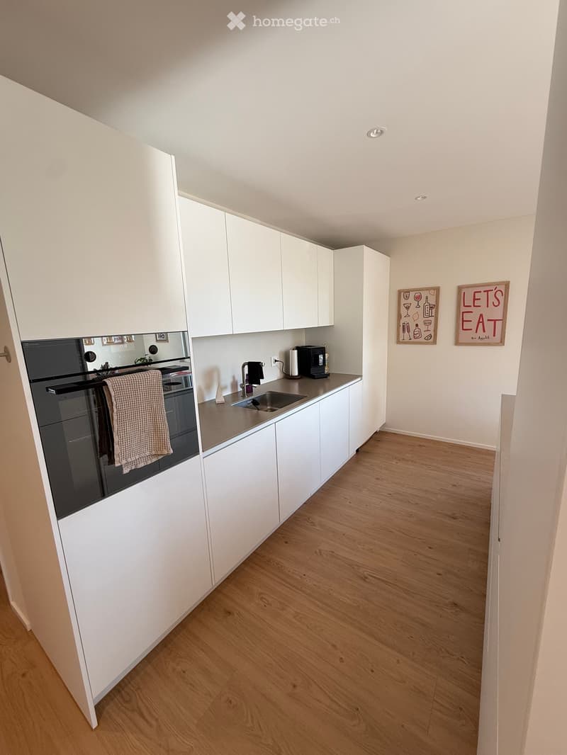 Modern kitchen with white cabinets, wooden flooring, stainless steel sink, oven, and coffee maker on the counter.