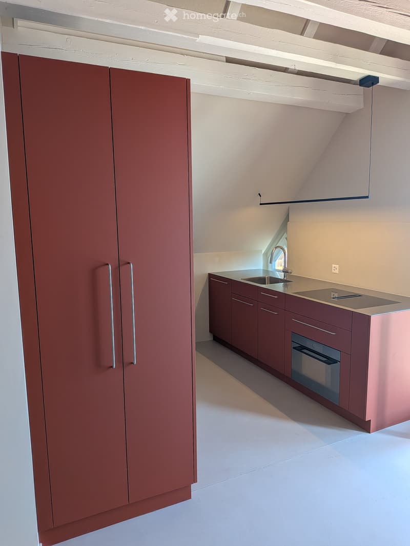 Modern kitchen with red cabinets, a sink, a faucet, and an oven. The space is well-lit with white walls and a clean, minimalist design.
