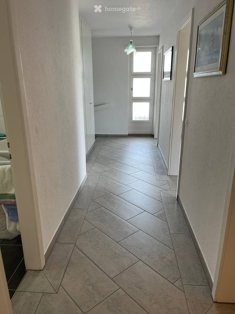 Clean, tiled hallway with light-colored walls, a hanging light fixture, and a door at the end.