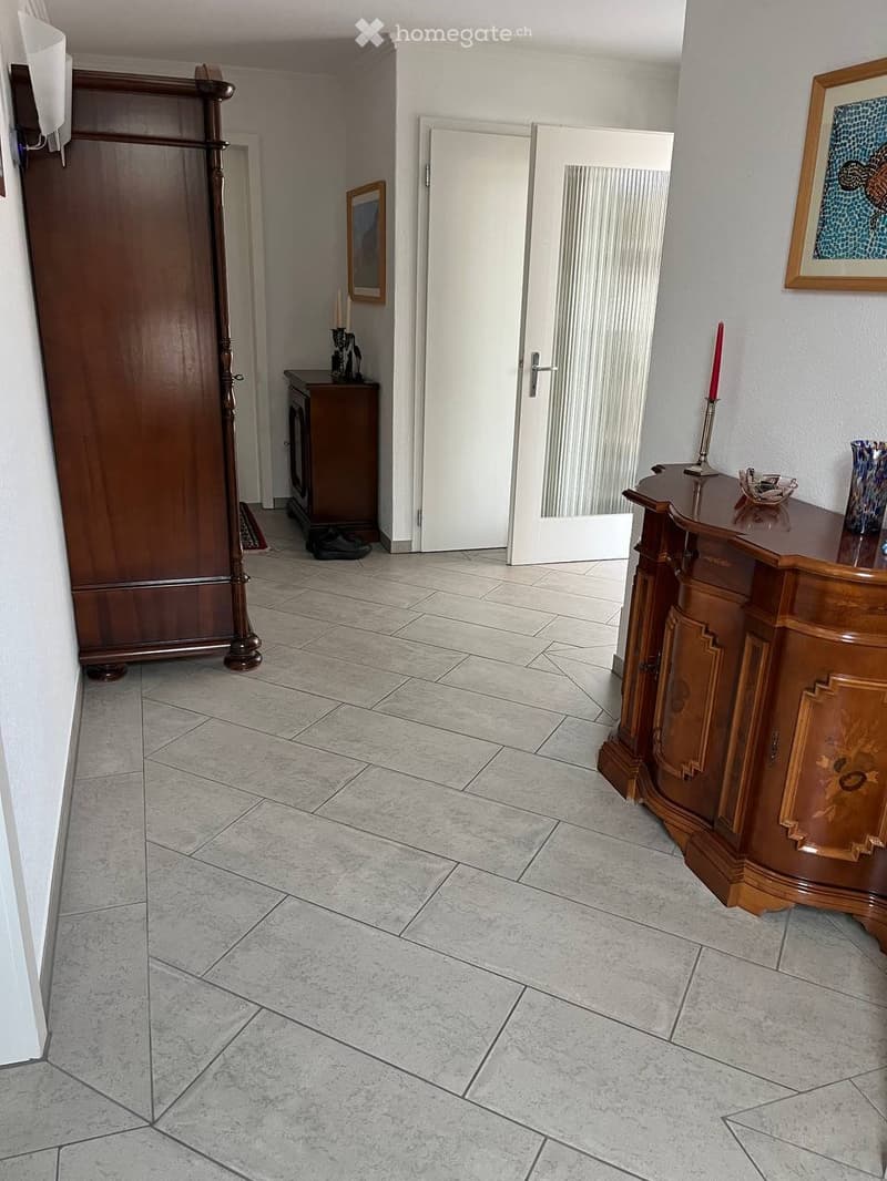 Hallway with tiled floor, wooden wardrobe, small wooden cabinet, and a door leading to another room.