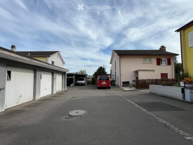 Residential street with two-story houses, garages, and parked vehicles.