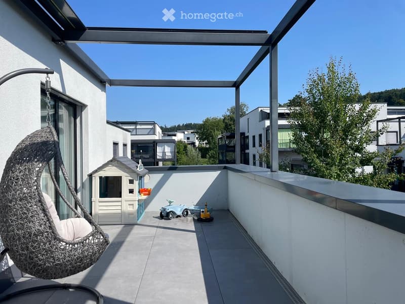 Modern rooftop terrace with a hanging egg chair, small playhouse, toy car, and a clear view of surrounding buildings and greenery.