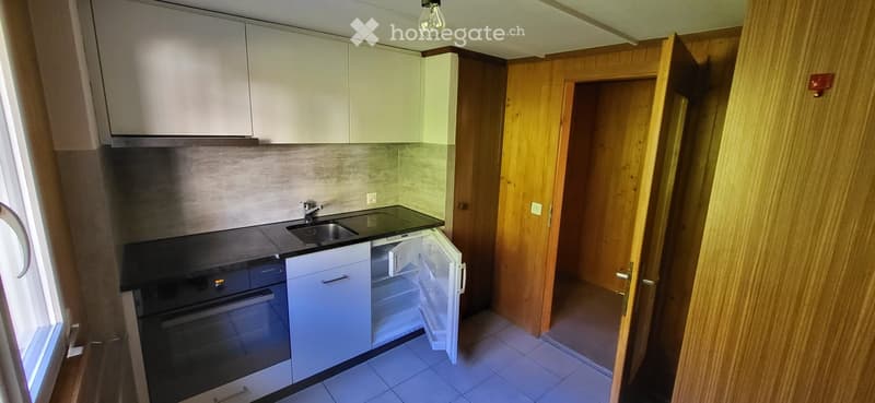Modern kitchen with white cabinets, stainless steel sink, oven, and open refrigerator. Wooden door leads to another room.