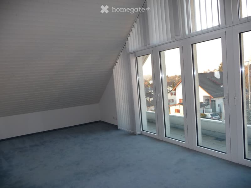 Empty room with grey carpeted floor, white walls, large glass sliding doors leading to a balcony, and a slanted ceiling.