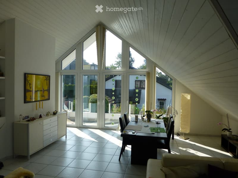 Bright, modern dining and living area with large windows and sliding glass doors leading to a patio. Features a dining table with chairs, a sofa, a cabinet with decorative items, and a picture frame on the wall.