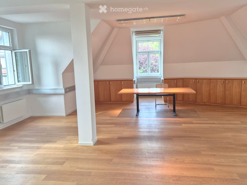 Bright, unfurnished room with wooden flooring, large windows, and built-in wooden cabinets.