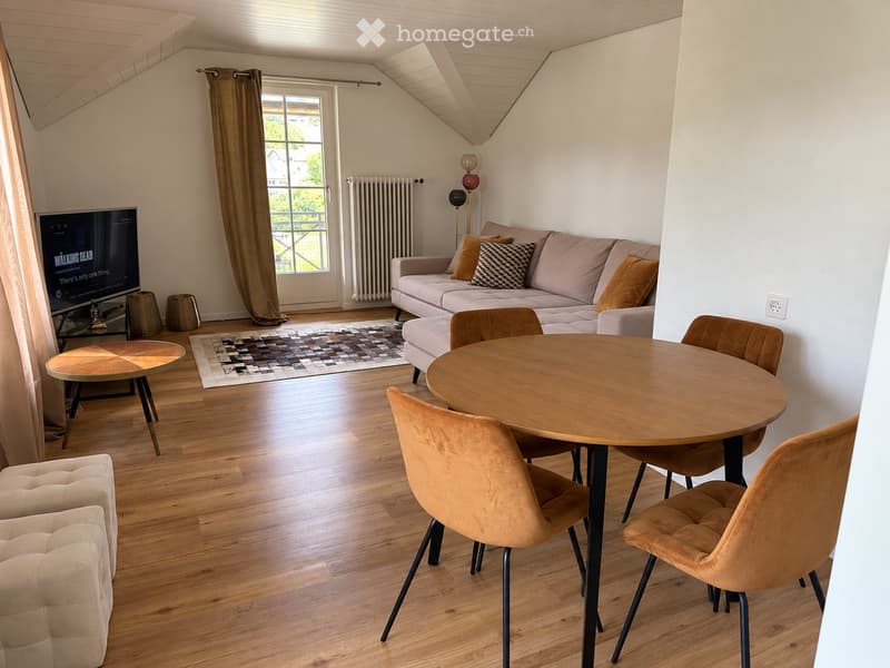 Modern living room with wooden flooring, a large sofa with throw pillows, a coffee table, a dining table with chairs, and a television on a stand.