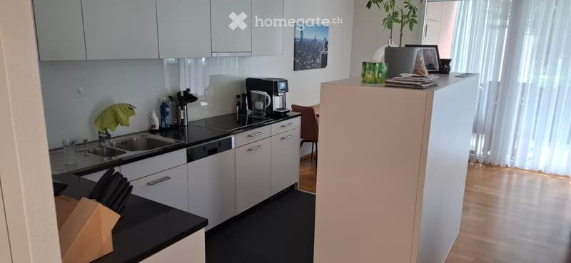 Modern kitchen with white cabinets, black countertops, stainless steel appliances, and a small dining area with a chair and table.