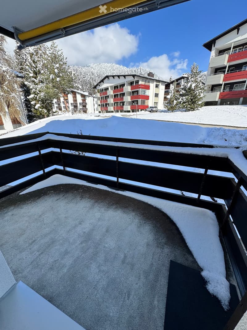 A snow-covered balcony overlooking a snowy landscape with buildings and trees in the background.