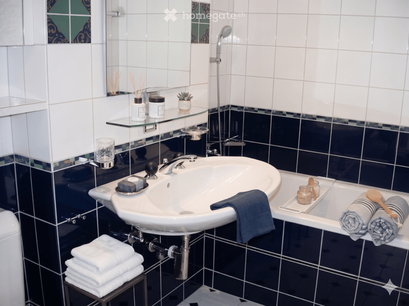 Bathroom. Modern bathroom with white tiles, dark blue lower tiles, a sink, bathtub, and neatly arranged towels and toiletries.