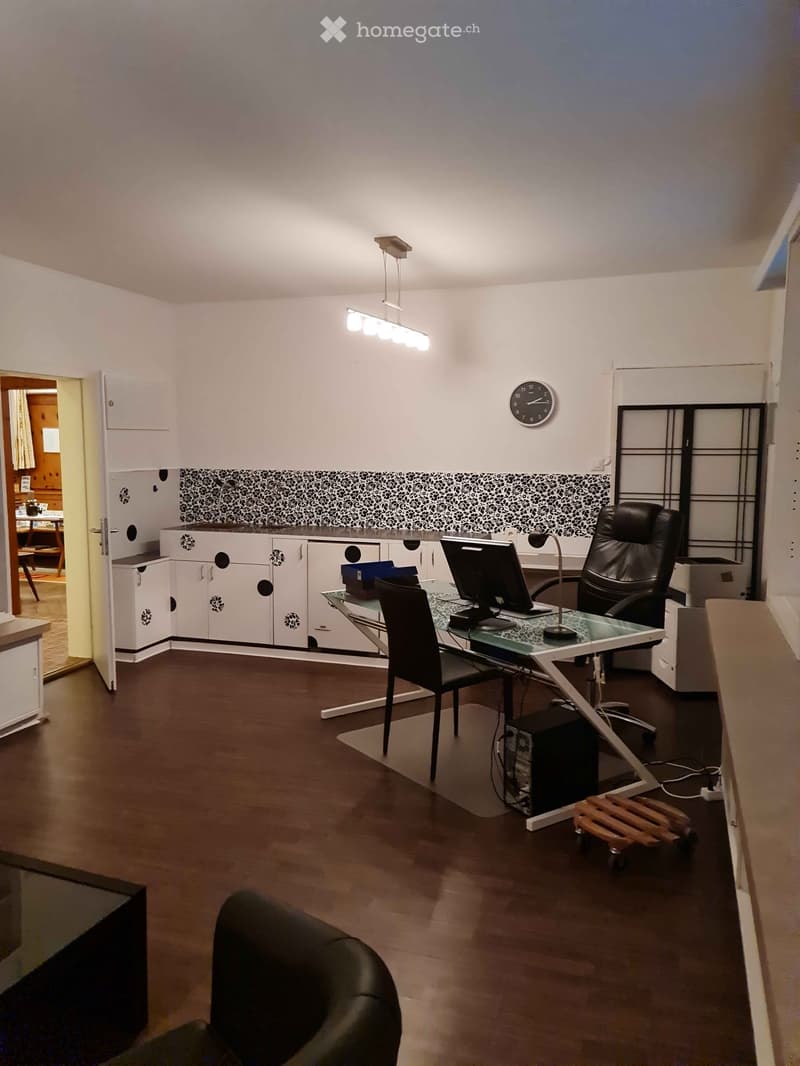 Office space with a glass desk, black leather chair, computer screen, cabinets, and a clock on the wall.