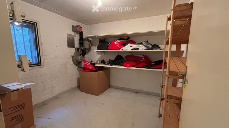 Empty room with white brick walls, concrete floor, shelves holding helmets and bags, a window with blinds, and a ladder leading to an attic or loft area.