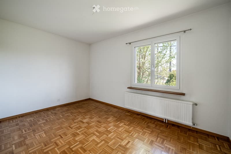 Empty room with wooden herringbone flooring, white walls, a large window with a radiator below, and a window sill. No furniture or equipment present.