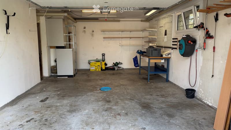 Empty garage with concrete floor, white walls, shelves, and various tools and equipment stored along the walls.