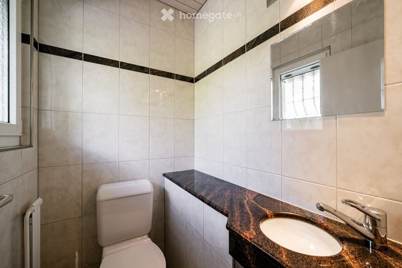 Modern bathroom with white tiles, a dark granite countertop, a single sink with a chrome faucet, a toilet, a mirror, and a small cabinet.