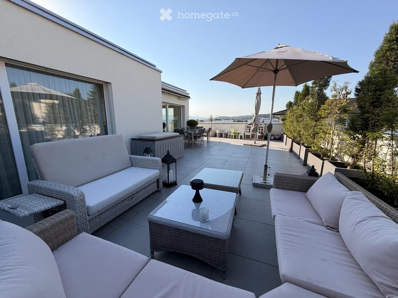 A modern rooftop terrace with white wicker furniture, including a sofa, coffee table, and umbrella, overlooking a cityscape.