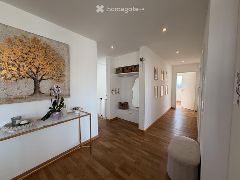Elegant hallway with wooden flooring, white walls, and modern decor including a glass console table, artwork, and framed pictures.