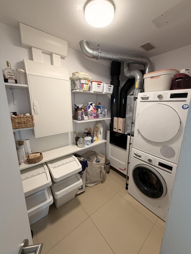 A compact laundry room with a washing machine, dryer, shelves, and cleaning supplies.