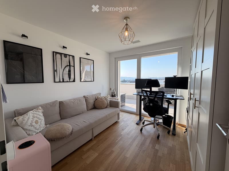 Modern living room with a sofa, a desk with a laptop, and a view of the sea through large windows.
