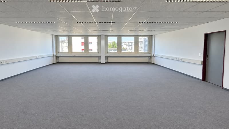 Empty room with grey carpet, white walls, large windows, and a door.