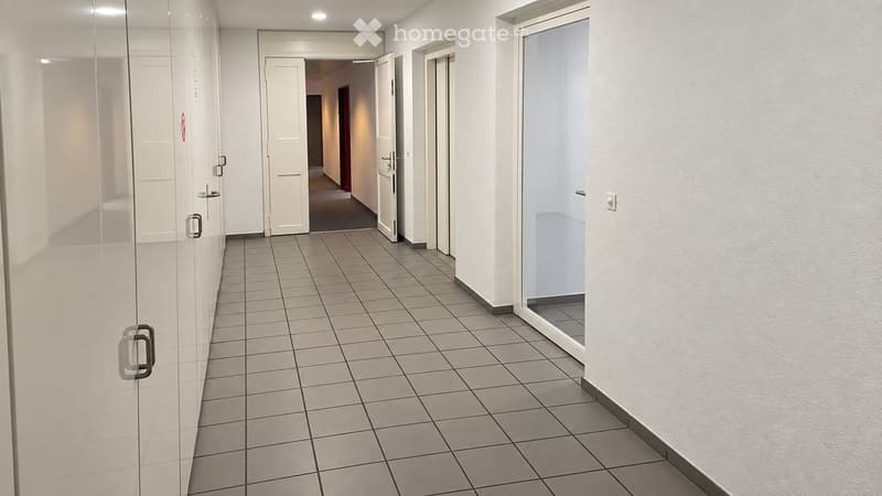 Clean, modern hallway with tiled flooring, white walls, and several doors including a glass-paned door on the left and a partially open door leading to another room.
