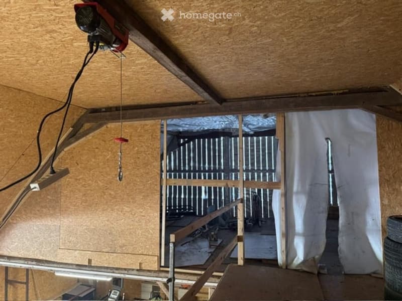 Empty attic space with exposed wooden beams, unfinished walls, and a metal staircase leading to another area. No furniture or equipment present.