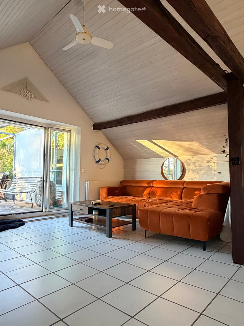 Bright living room with white tiled flooring, orange sectional sofa, coffee table, and a round mirror on the wall. Large sliding glass doors lead to an outdoor area.