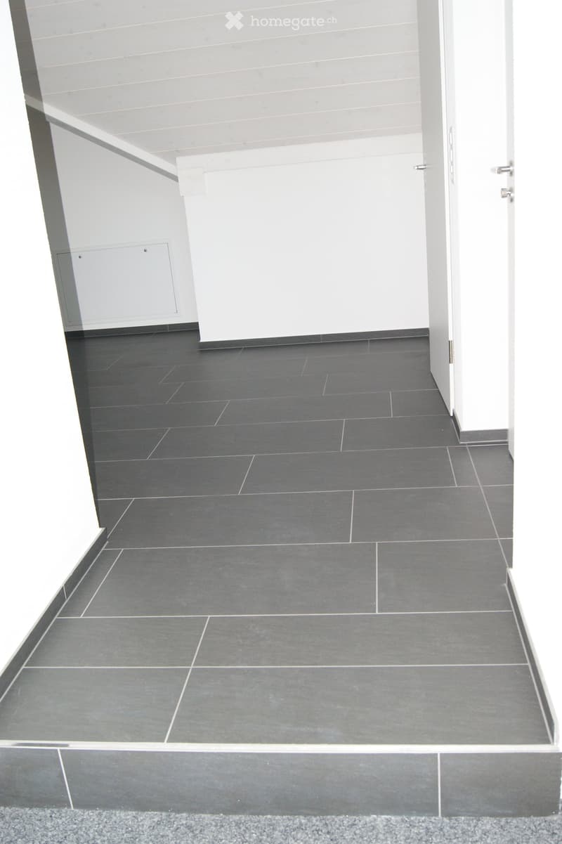 Modern hallway with grey tiled floor, white walls, and raised platform at the entrance.