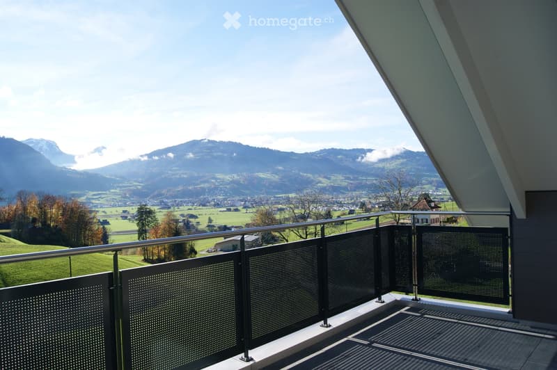 Balcony with metal railing, overlooking a scenic valley and mountain range.