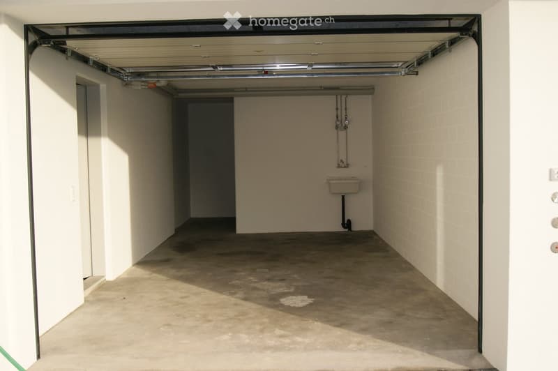 Empty garage with concrete floor, white tiled walls, and a small utility sink in the corner.