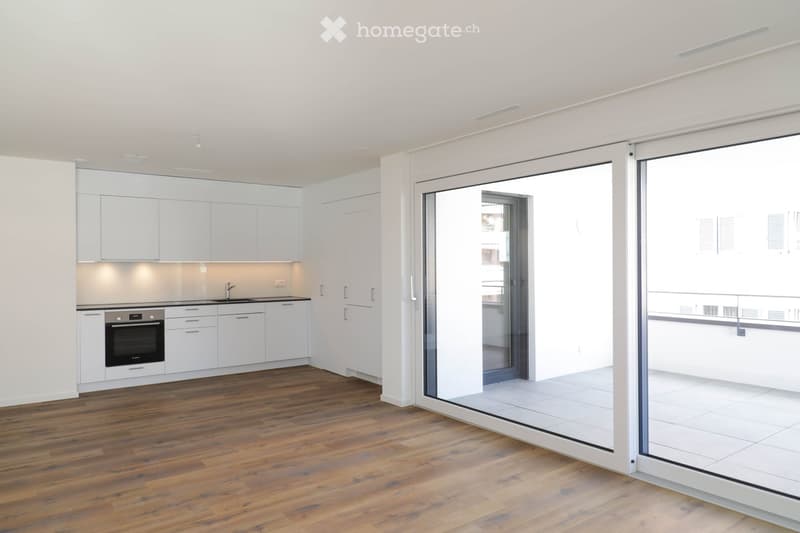 Modern kitchen with white cabinets, wooden flooring, and a large glass sliding door leading to a tiled area.
