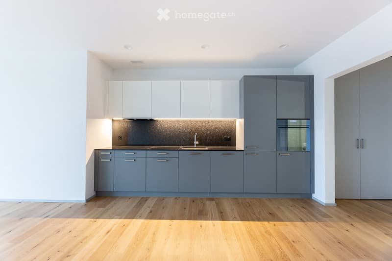 Minimalist modern kitchen with wooden flooring, white upper cabinets, gray lower cabinets, sink, dishwasher, stove, wooden countertops