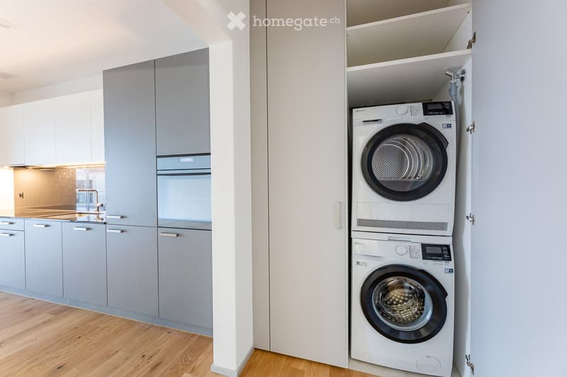 kitchen area, washing machine stacked, gray cabinets, wooden floor, sink with faucet