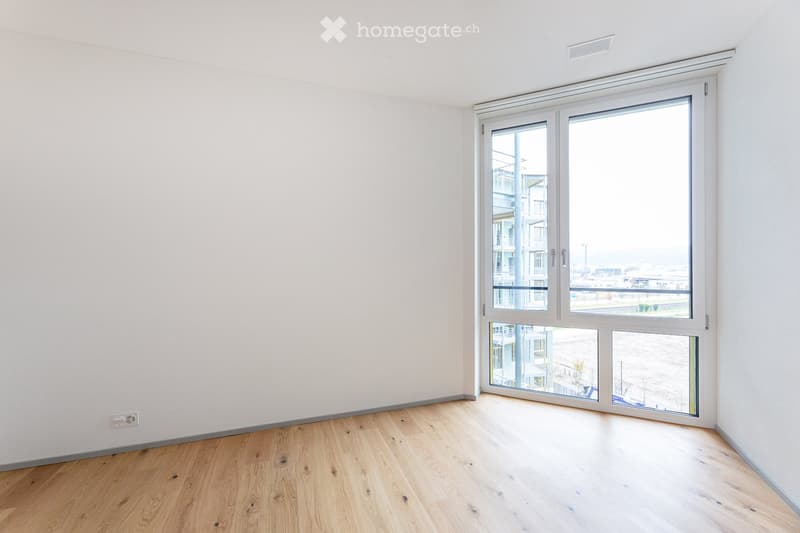 Empty room with white walls, hardwood floors, large glass windows with view of outside