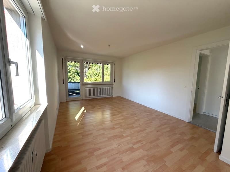 Empty room with wooden flooring, white walls, large windows, and a radiator. No furniture or equipment present.
