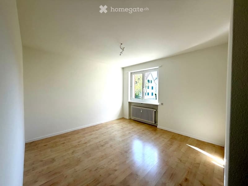 Empty room with wooden flooring, white walls, and a single window with a radiator below it.