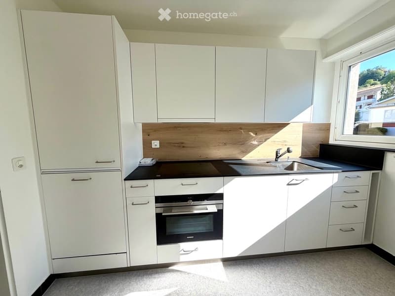Modern kitchen with white cabinets, black countertops, and built-in appliances including an oven and sink.