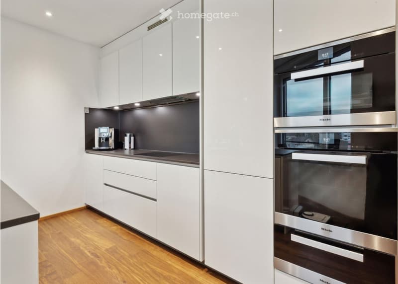 Modern kitchen with white cabinets, dark countertops, and a built-in oven. Features include a coffee machine on the counter and sleek, contemporary design.