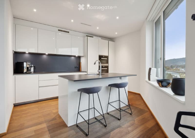 Modern kitchen with white cabinets, a central island, and a large window offering a scenic view. Features include a coffee maker, stools, and decorative vases on the windowsill.