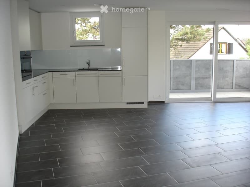 Modern kitchen with white cabinets, dark tiled floor, and a large window overlooking a house and garden.